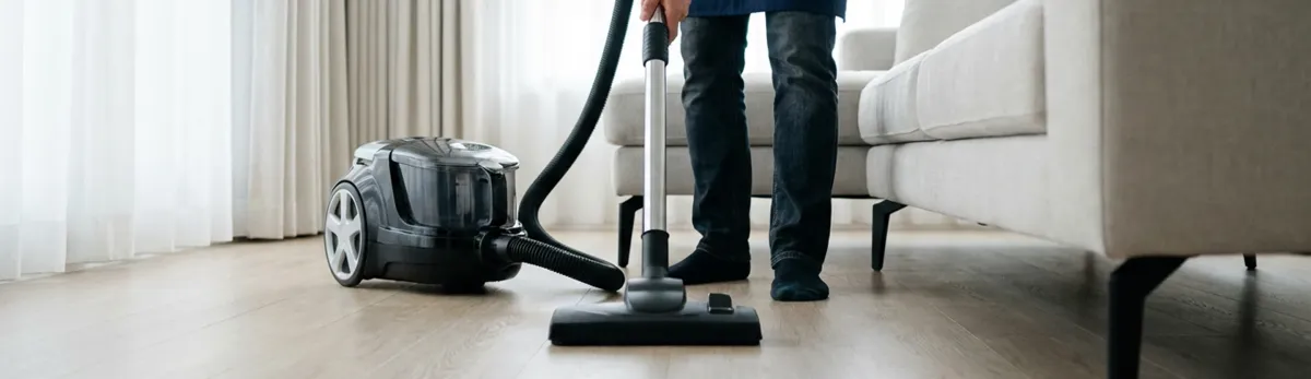 Professional house cleaner vacuuming a living room floor with a canister vacuum cleaner, Tallahassee, FL.
